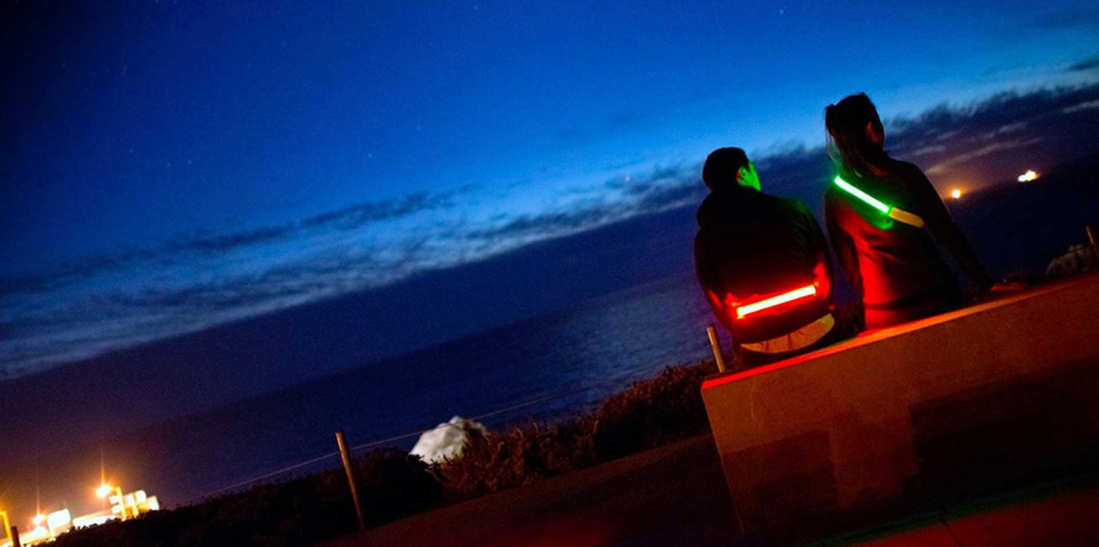 Deux personnes assises au bord de l'eau la nuit, portant une ceinture et un harnais lumineux